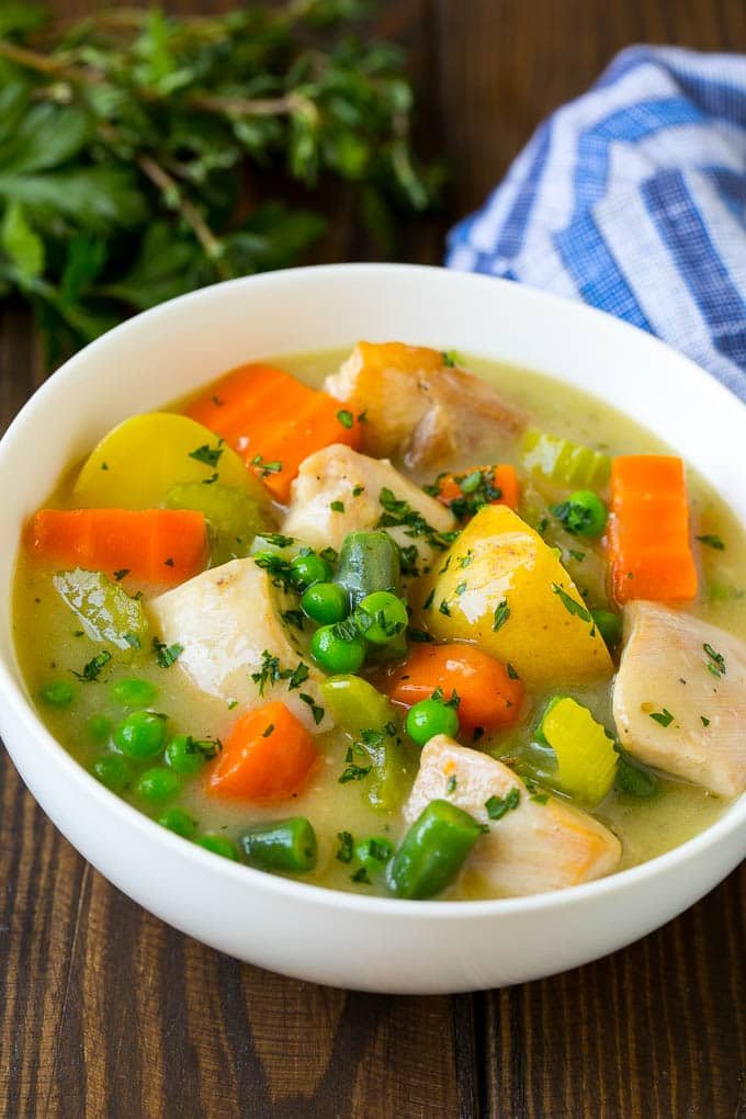 A bowl of chicken stew with celery, potatoes, green beans and peas.