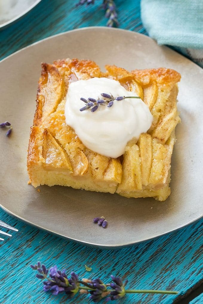 A slice of apple cinnamon cake on a small plate topped with whipped cream.