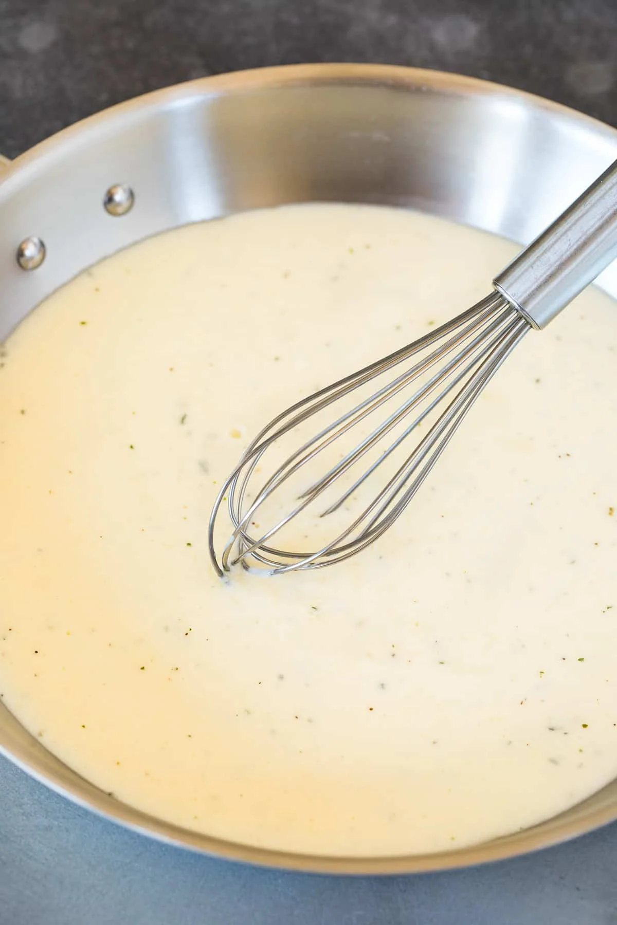 A pan of creamy sauce with a whisk in it.