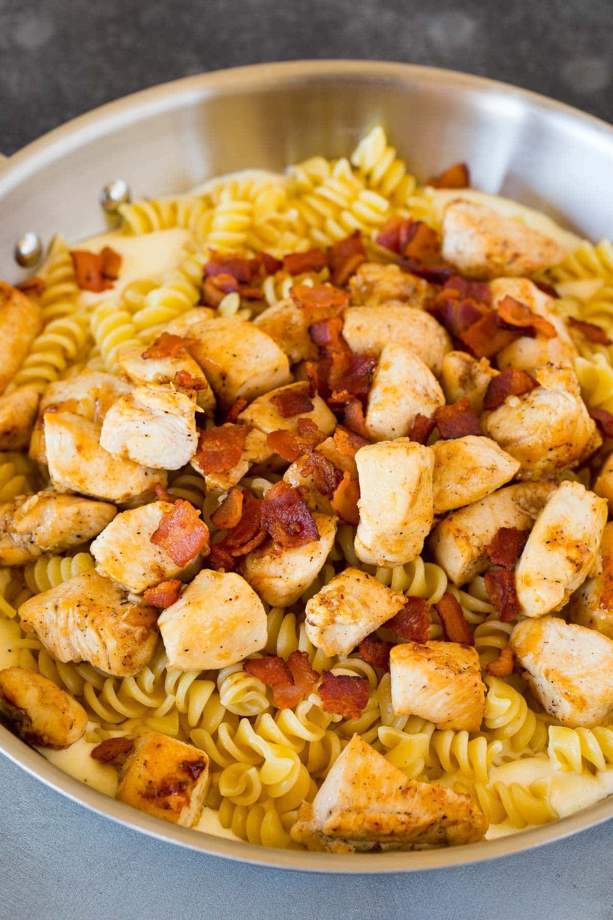 Chicken, rotini pasta and bacon in a pan of cream sauce.