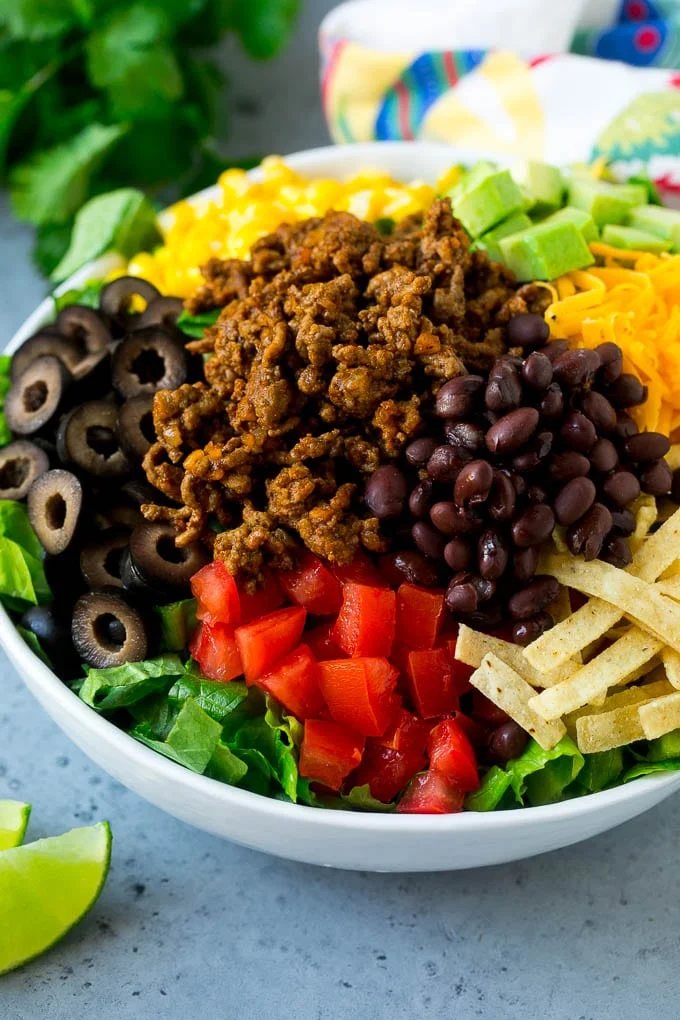 Ground beef, tortilla strips, beans, tomatoes, olives, corn and avocado over lettuce.