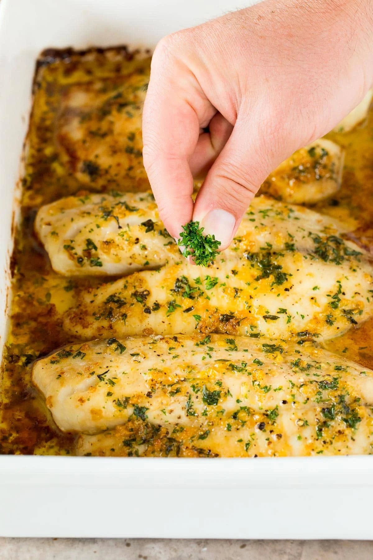 A hand sprinkling parsley over fish.