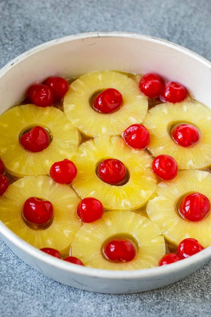 Pineapple rings and cherries at the bottom of a cake pan.