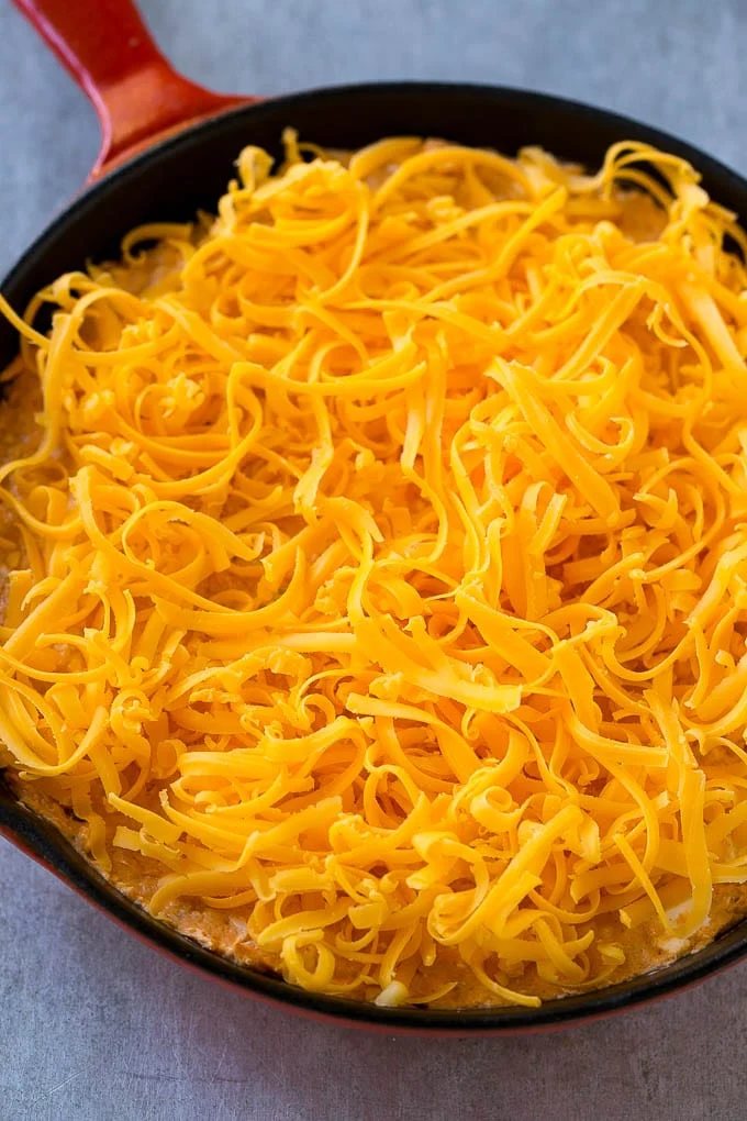 Buffalo chicken dip topped with shredded cheddar cheese, ready to go into the oven.