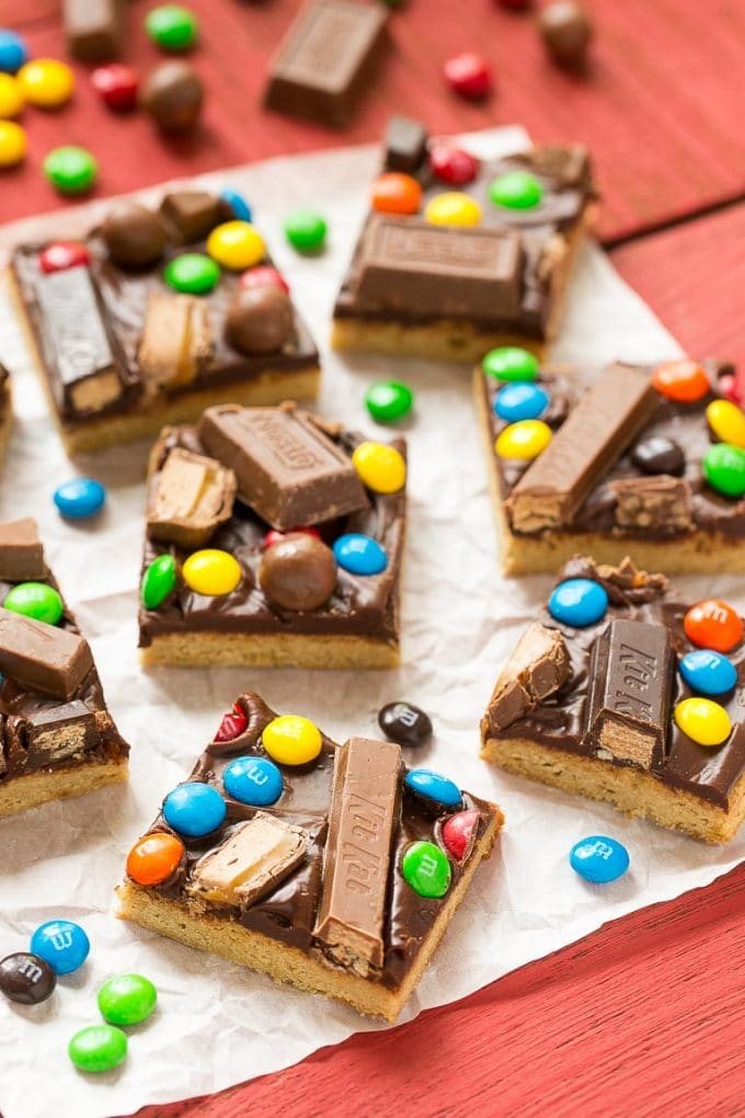 Several candy bar blondies featuring a blondie base, chocolate ganache and candies on top.