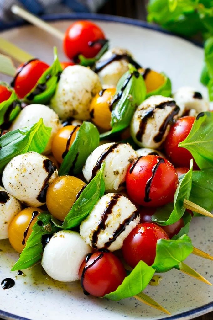 A plate of caprese skewers with mozzarella, tomatoes and basil.