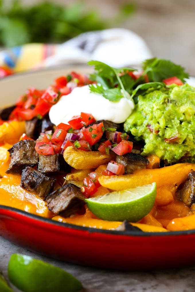 Carne asada fries in a skillet topped with sour cream, pico de gallo and steak.