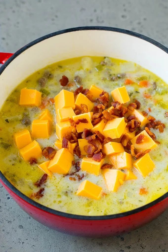 Potato soup base with cubes of Velveeta cheese and bacon being stirred in.