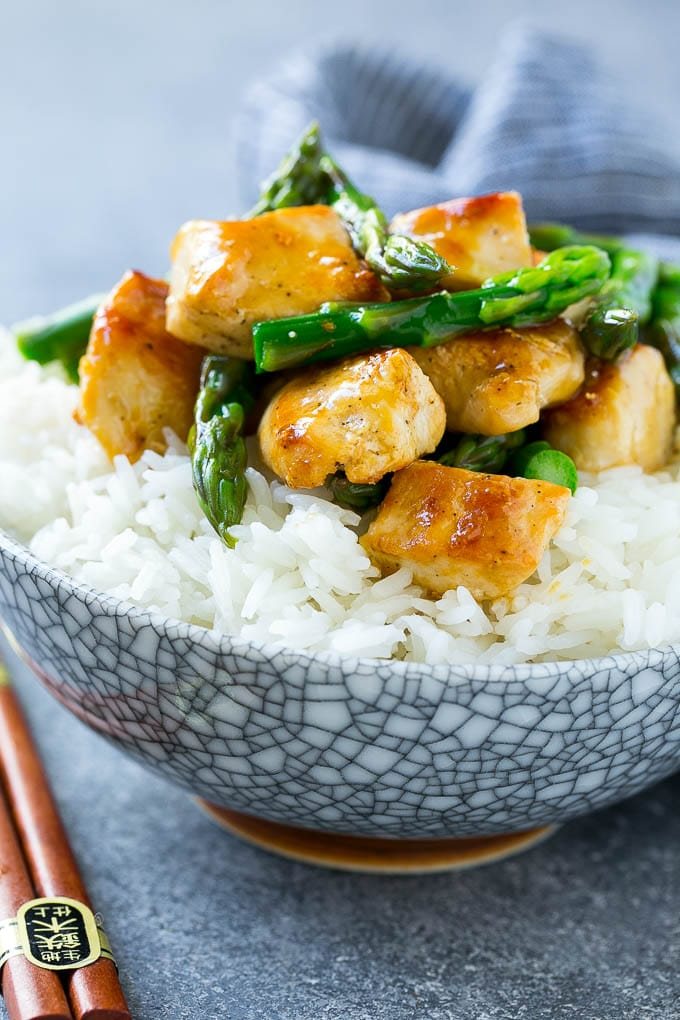 A bowl of chicken and asparagus stir fry served over steamed rice.