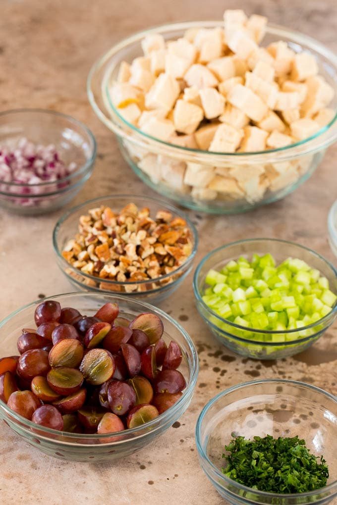 Bowls of diced chicken, celery, pecans, grapes, red onions and parsley.