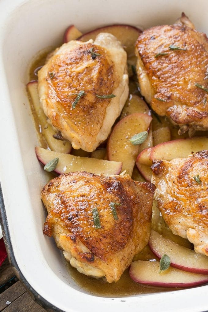 A dish with four apple cider glazed chicken thighs served over apples.