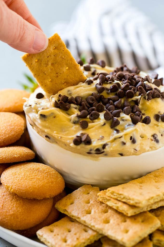 A graham cracker dipping into a bowl of cookie dough dip.
