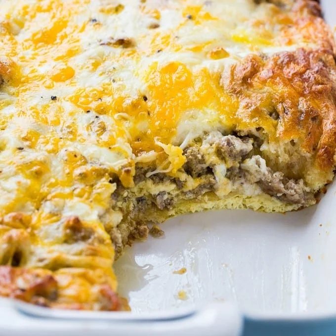 An image of a sausage and crescent roll casserole in a baking dish with a scoop removed.