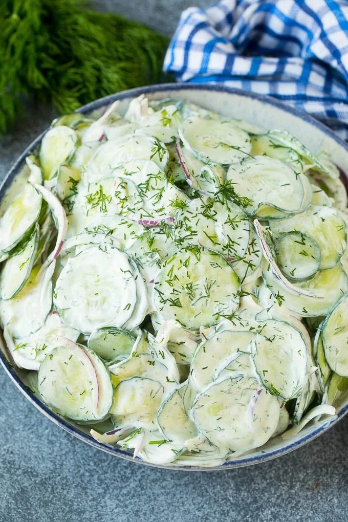 Silky cucumber salad with red onion and dill, topped with fresh herbs for garnish.