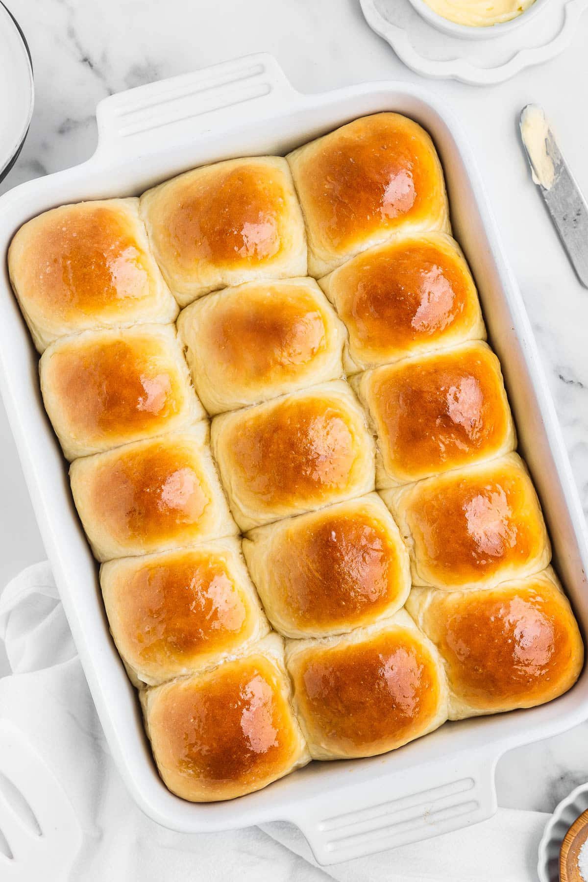 A pan of kitchen-made dinner rolls with butter and a knife on the side.
