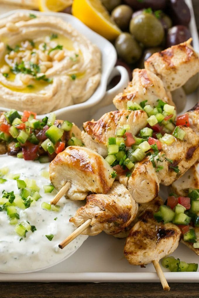 A tray of chicken souvlaki kabobs with olives, hummus, pita bread and yogurt sauce.