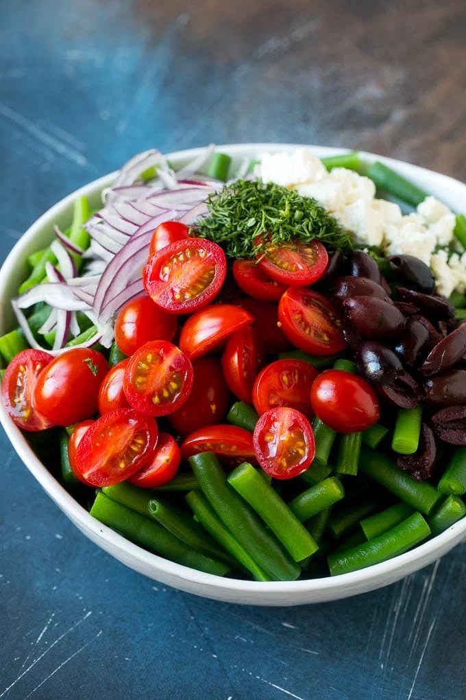 Vegetables like cherry tomatoes, red onion and olives in a bowl with feta cheese.