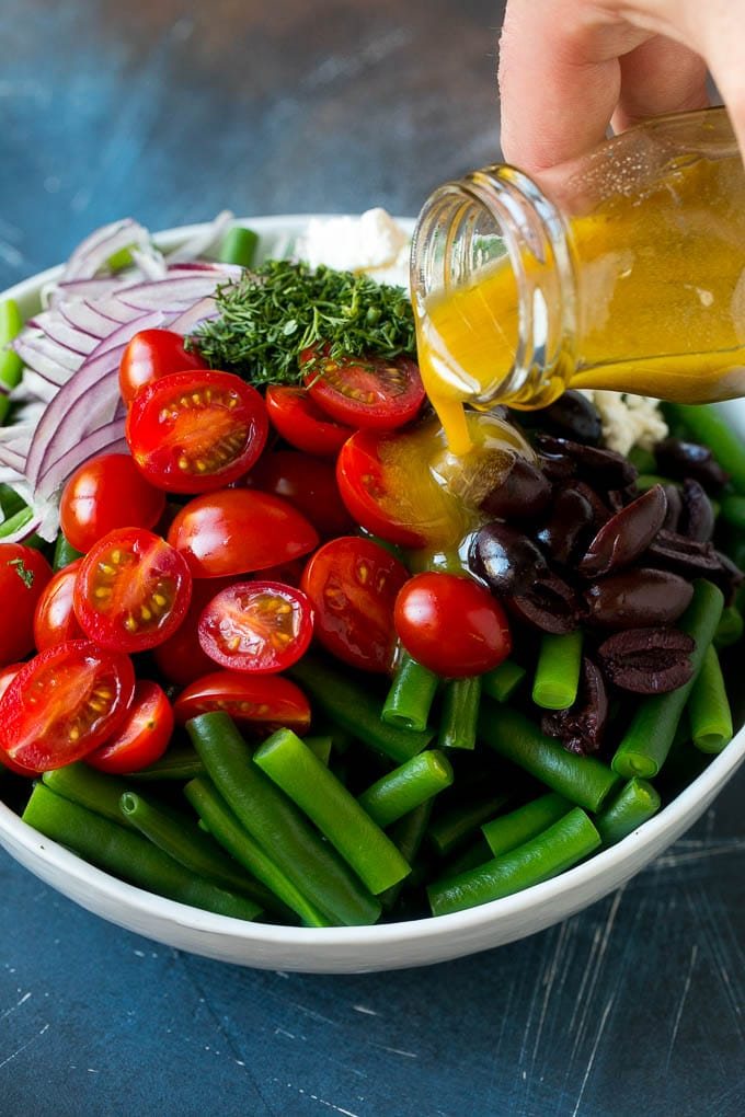 Dressing being poured over veggies like cherry tomatoes, olives and onions.
