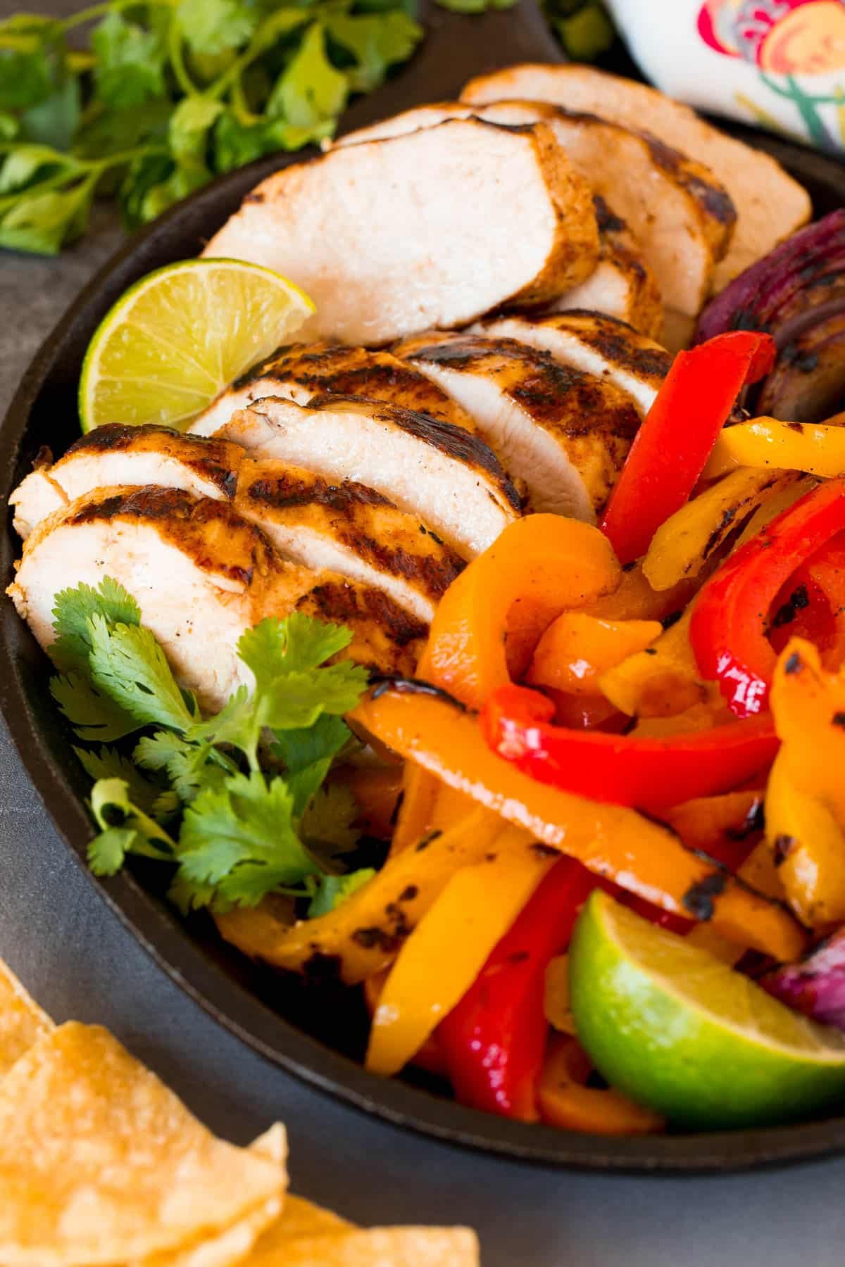 Grilled chicken fajitas with sliced cooked chicken, colorful peppers and lime wedges.