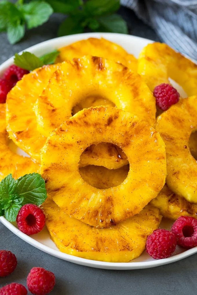 A plate of grilled pineapple slices garnished with raspberries and mint.
