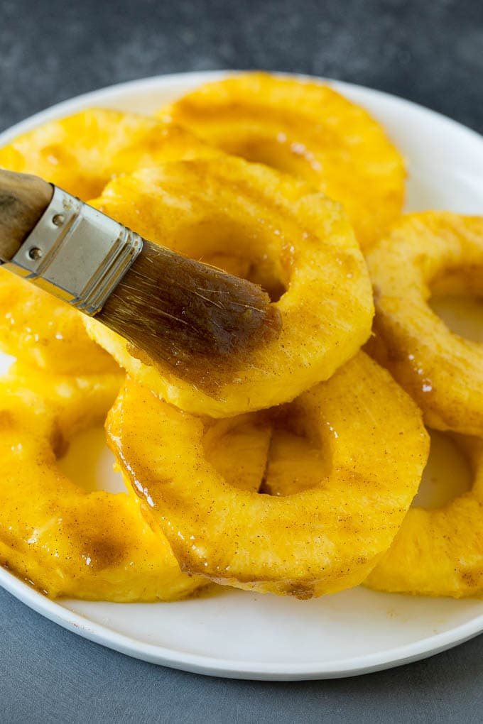 A brush coating fruit slices with butter and brown sugar.