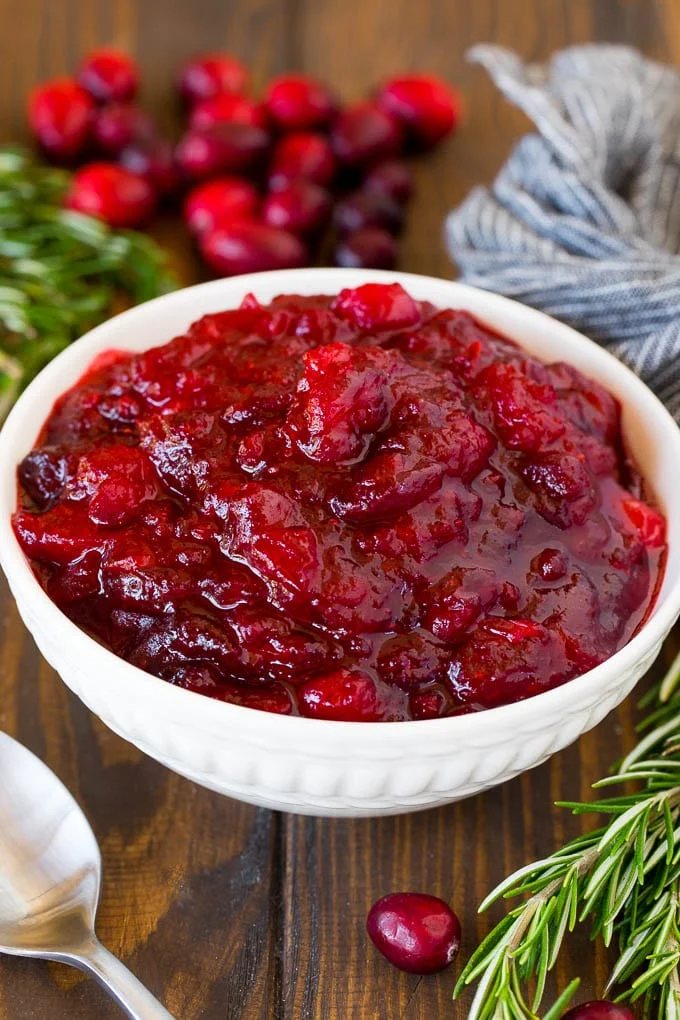 A bowl of kitchen-made cranberry sauce with a serving spoon and garnishes.