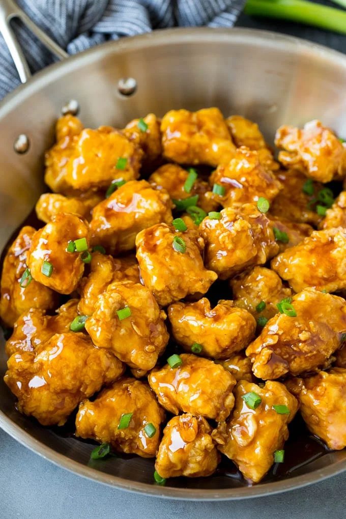 A pan of crunchy honey chicken garnished with green onions.