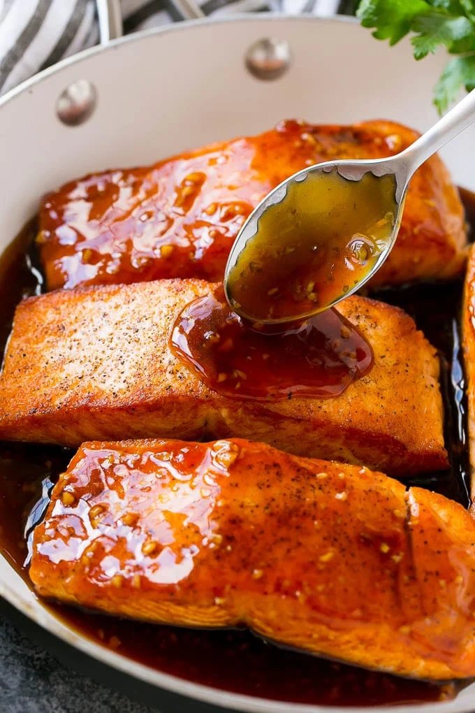 A spoon pouring sauce on top of salmon fillets.