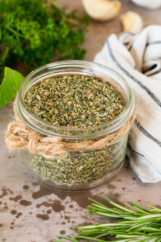 A jar of kitchen-made Italian seasoning surrounded by fresh herbs.