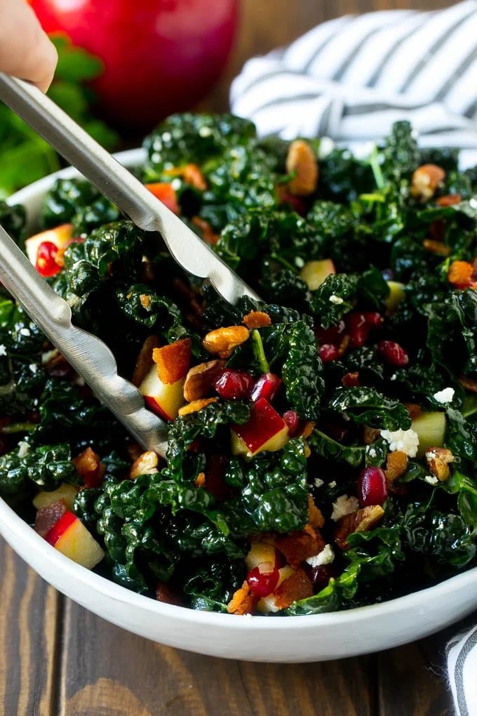 Tongs in a bowl of kale and apple salad.