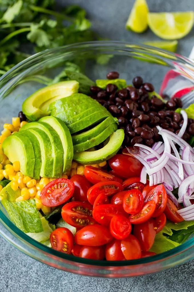 Lettuce, tomatoes, onion, corn, avocado and black beans in a bowl.