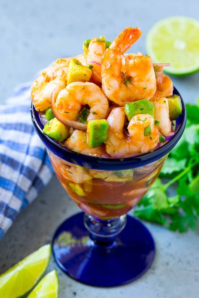 An individual cup of Mexican shrimp cocktail with red onion and avocado.