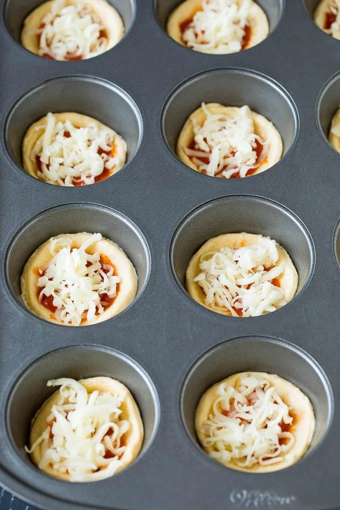 Circles of dough topped with pizza sauce and shredded cheese.