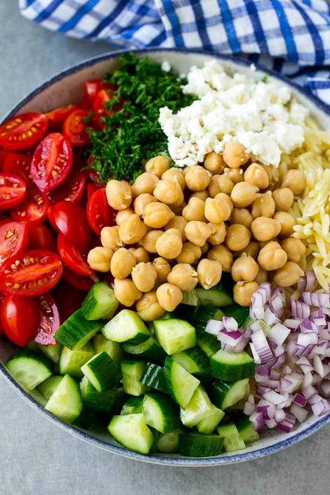 A bowl of pasta, cucumbers, cherry tomatoes, feta cheese, red onions, herbs and chickpeas.