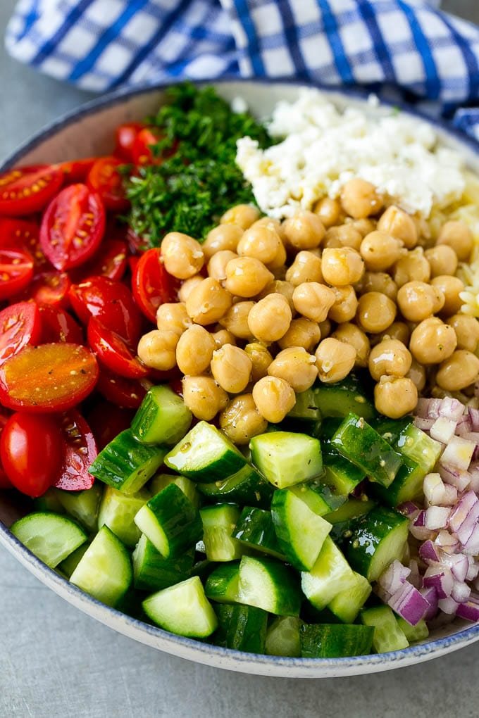 A bowl of pasta, tomatoes, cucumbers, red onions, chickpeas and feta cheese topped with dressing.