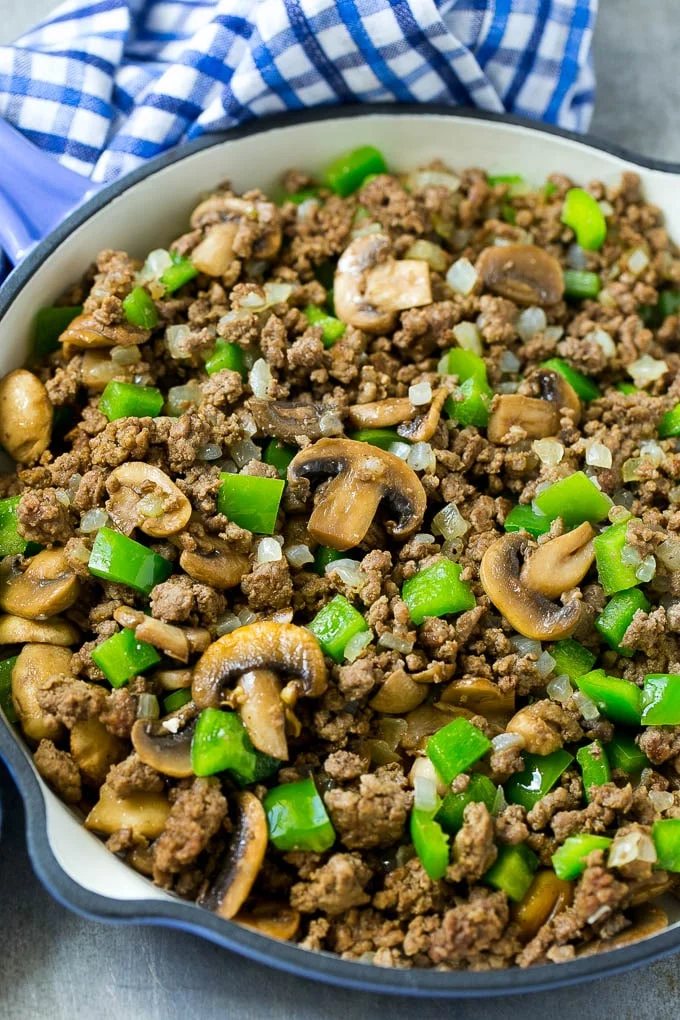A skillet of browned hamburger meat, mushrooms, onions and bell peppers.