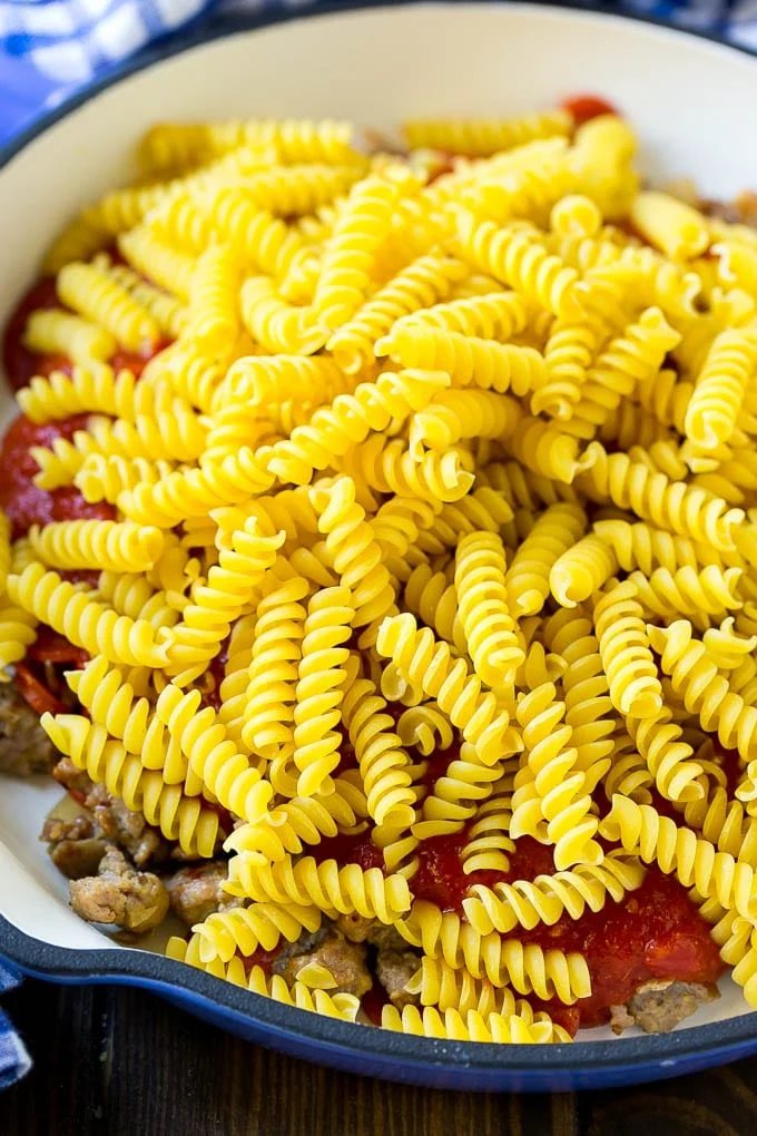 Pepperoni, sausage, tomato sauce and uncooked pasta in a skillet.