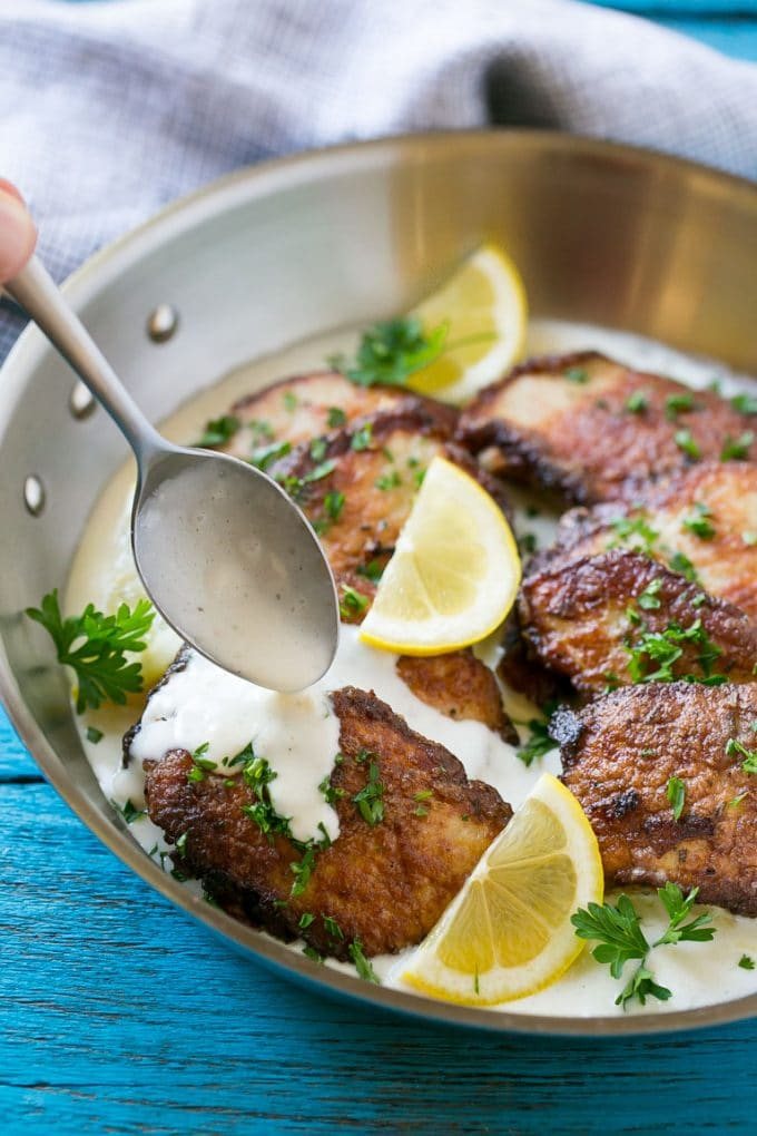 Pork scallopini in a pan with a spoon drizzling silky sauce over the top.