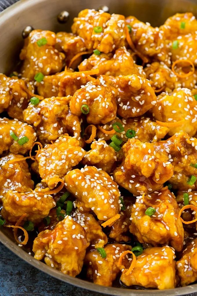 Orange chicken in a skillet with crunchy chicken, sesame seeds, orange zest and green onions.