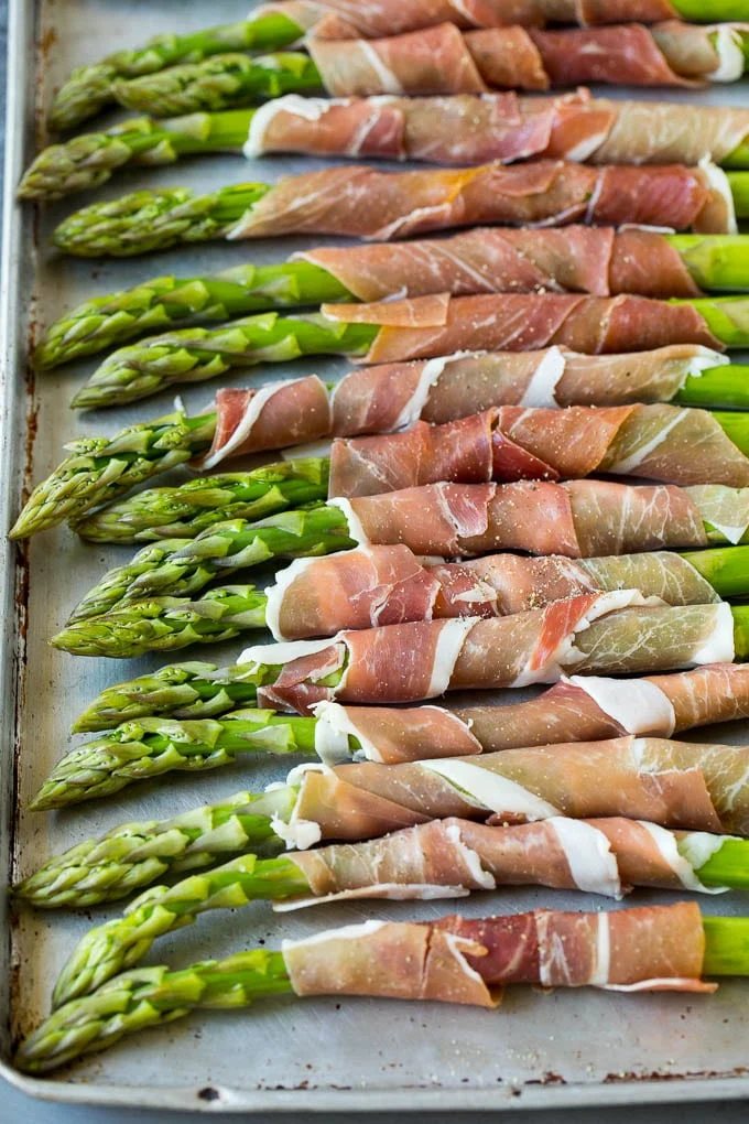 Asparagus on a sheet pan with prosciutto, ready for the oven.