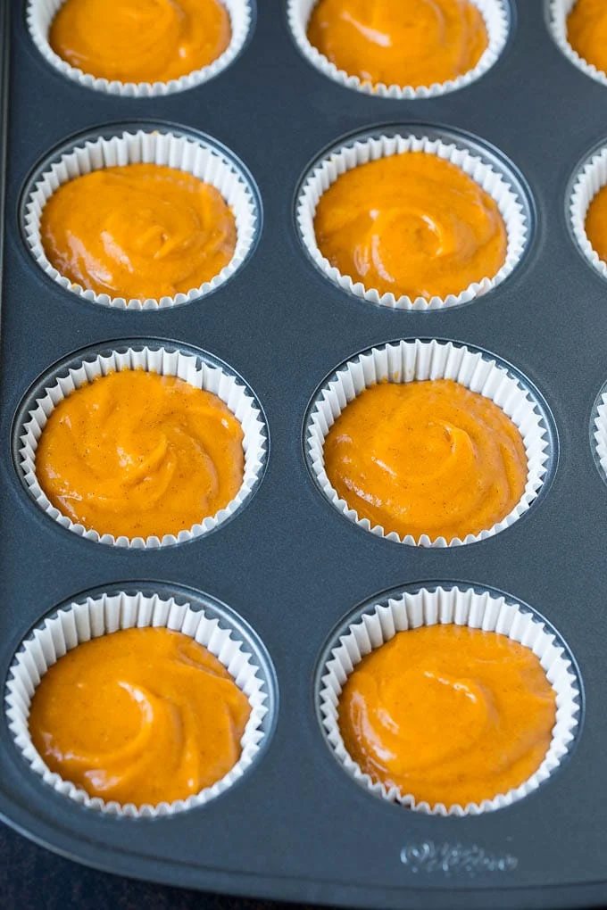 Batter inside paper cups in a muffin tin.