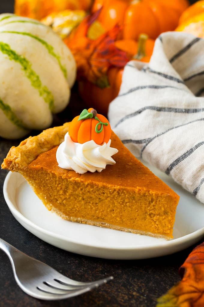 A slice of kitchen-made pumpkin pie topped with whipped cream and a candy pumpkin.