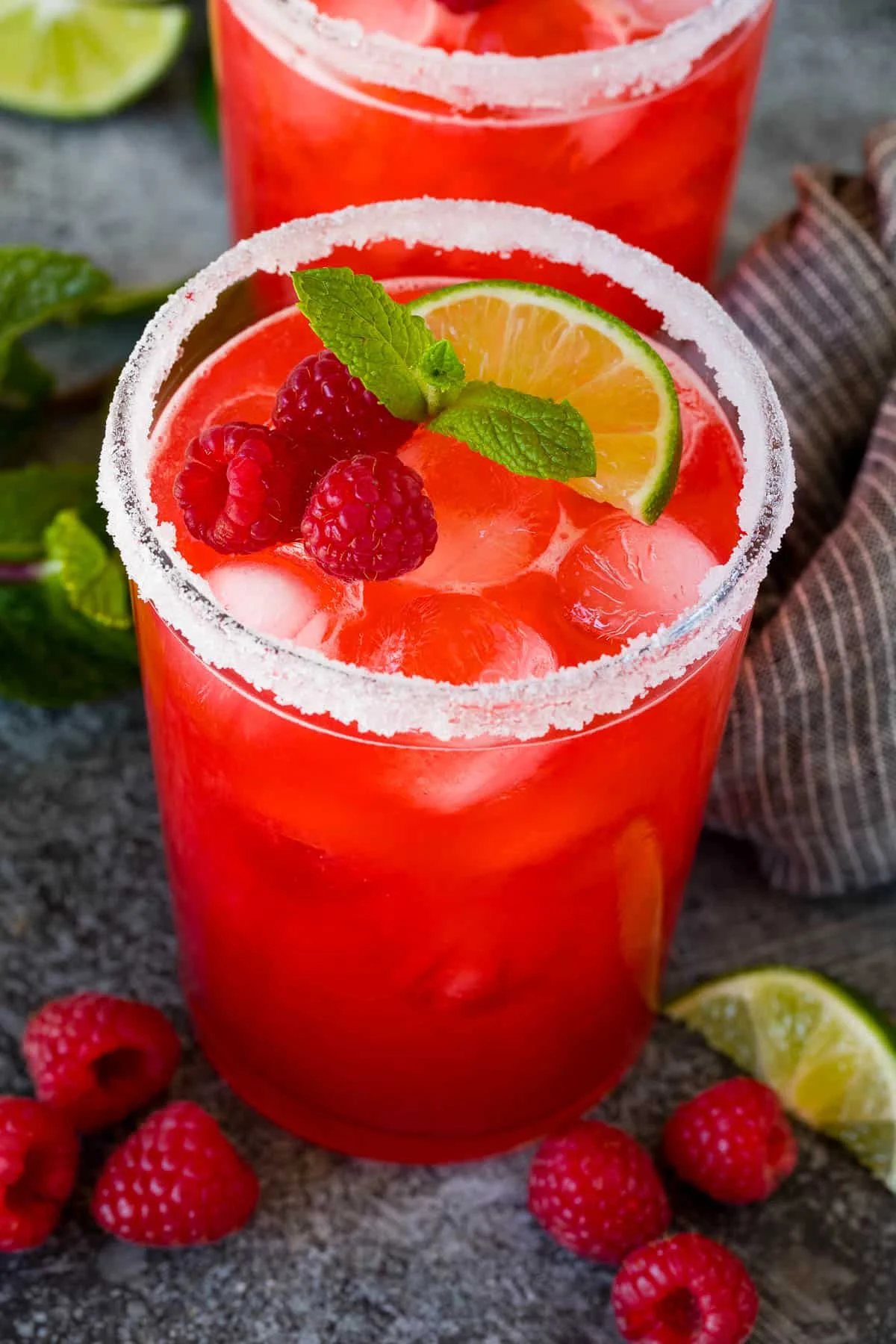 Glasses of raspberry margarita garnished with berries, mint and lime.