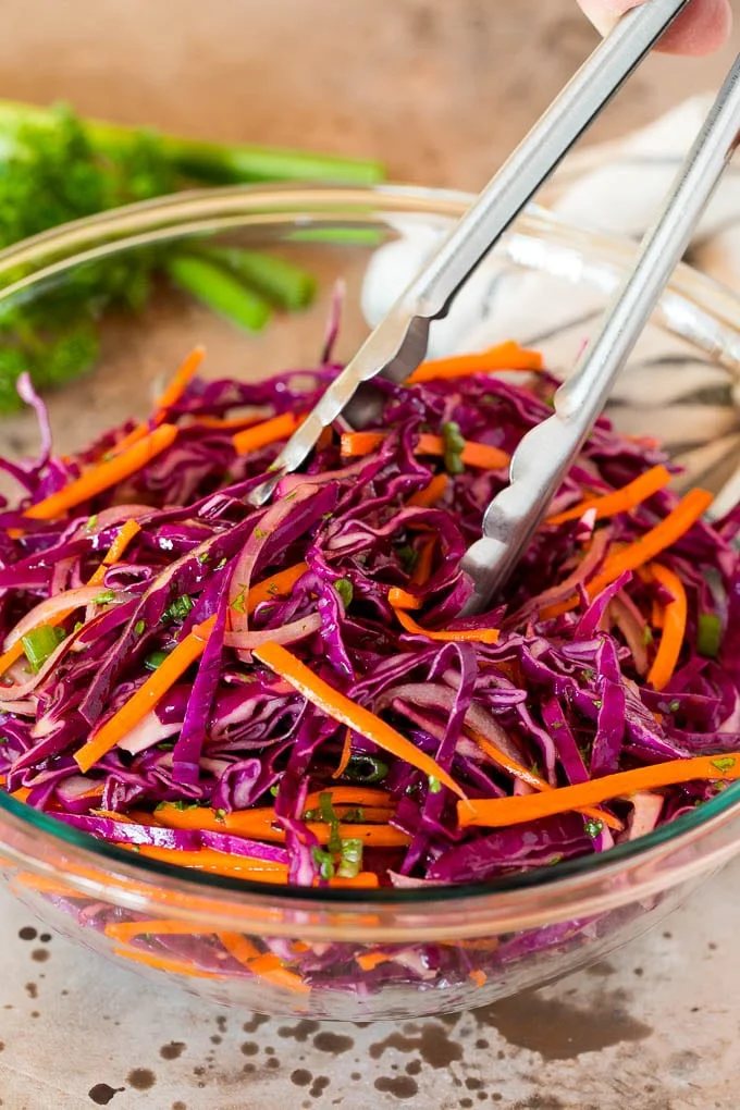 Tongs serving up a portion of red cabbage slaw.