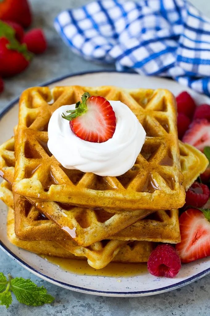 A stack of buttermilk waffles topped with syrup, whipped cream and fresh fruit.