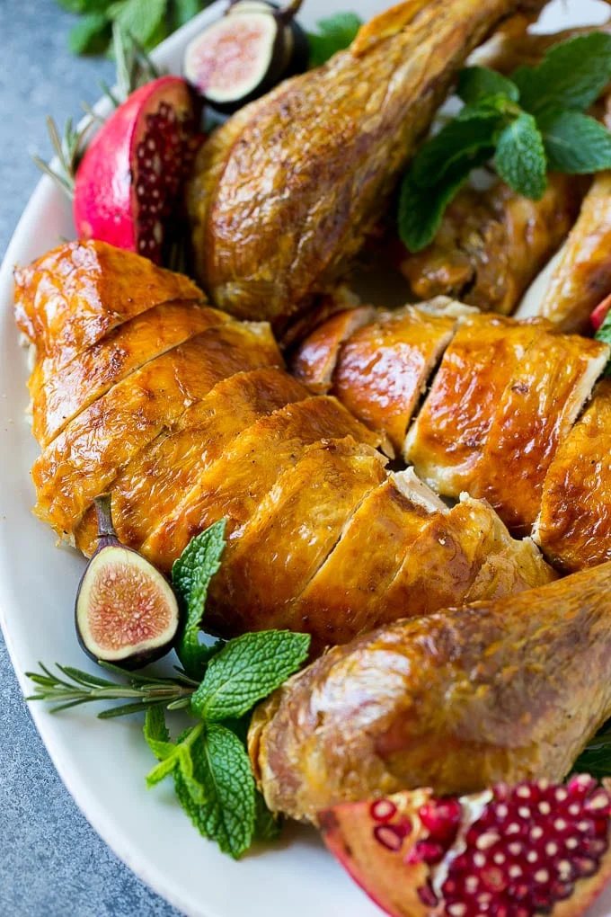Sliced roast turkey on a serving platter with rosemary, pomegranate and figs.
