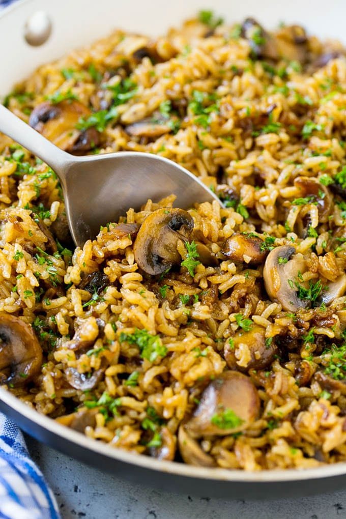 A skillet of straightforward mushroom rice with a serving spoon in it.