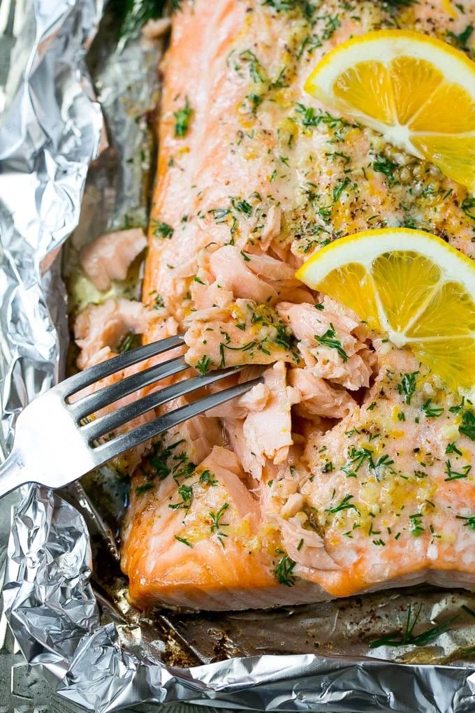 A fork cutting into a salmon filet that's been cooked in foil with garlic and herbs.