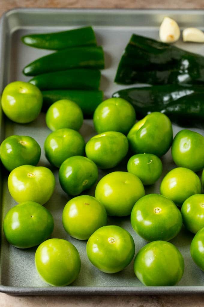 Tomatillos and halved peppers on a sheet pan.
