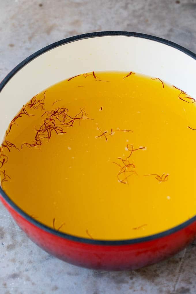 A pot of broth with saffron threads in it.